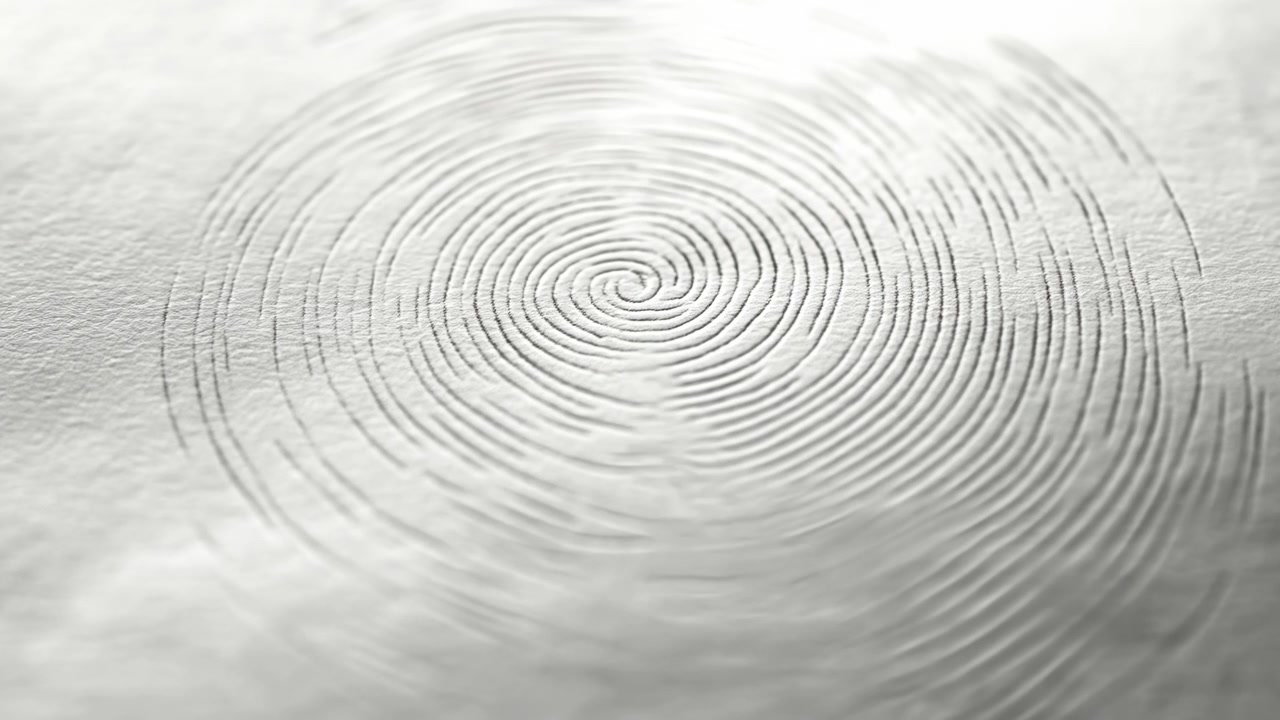 Camera advances toward centered spiral pattern pressed into a light textured surface, progressively enlarging curved ridges while shallow shadows emphasize relief and tactile detail.