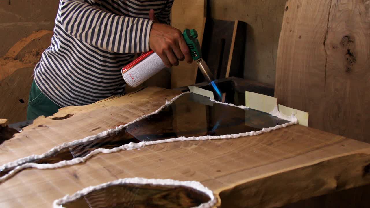 Closeup carpenter removing air bubbles with blowtorch from epoxy table