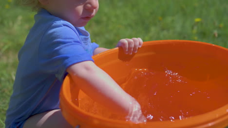 toddler joyfully plays and splashes water from a bucket on a hot, bright summer day