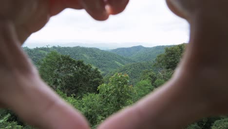 hands with fingers put together forming a heart revealing the mountains and forest showing lands and head of a woman