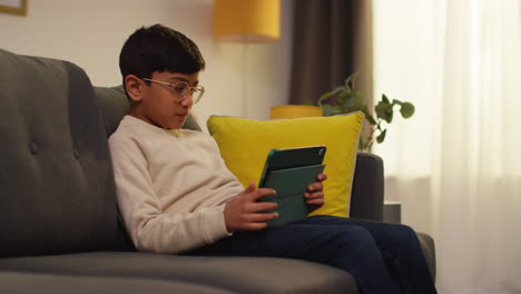 niño va a sentarse en el sofá en casa y jugar juegos o transmitir contenido a la tableta digital