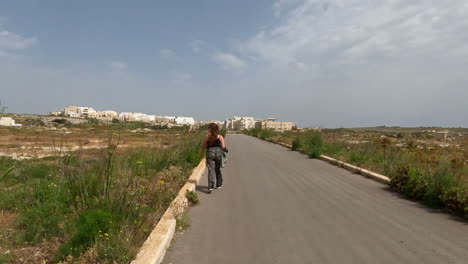 Woman-walking-on-asphalt-road-in-arid-landscape