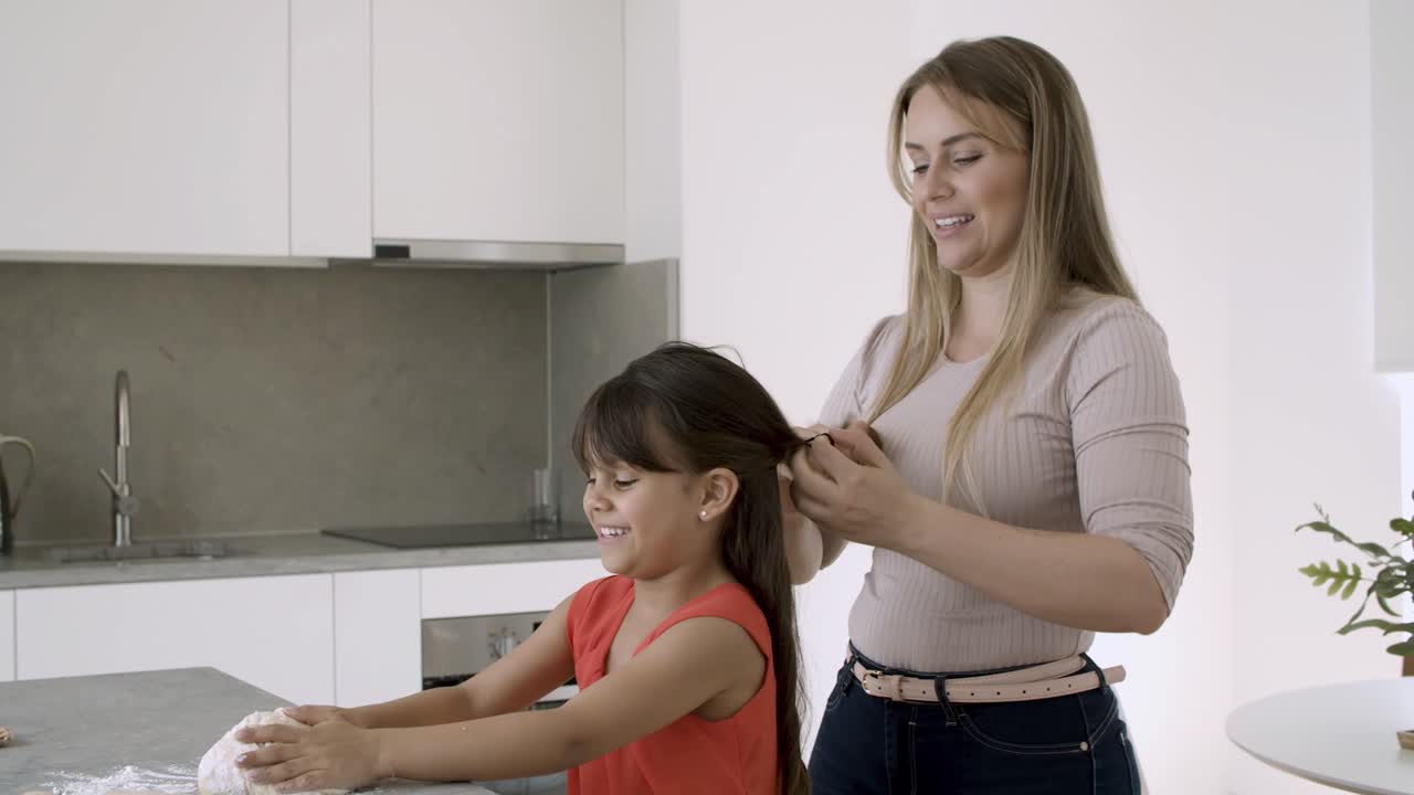 madre feliz trenzando hijas cabello largo