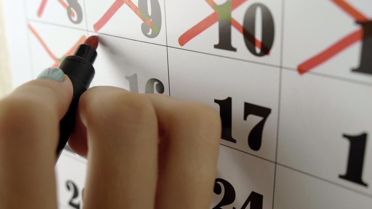 la mano de la mujer cruza con marcador rojo el día 16 del calendario. fotografía en cámara lenta.