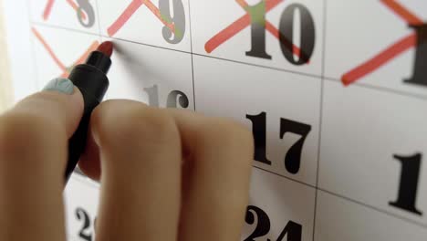 female hand crosses with red marker the calendar day 16. slow motion shot. close up