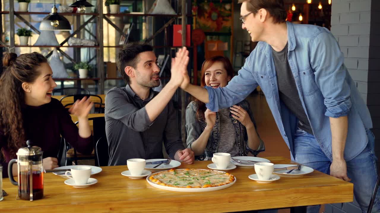 캐주얼 옷을 입은 기쁜 남자가 카페에 갑자기 도착한 젊은 여자를 놀라게 하고, 소녀는 소리치고 웃으며 흥분합니다.