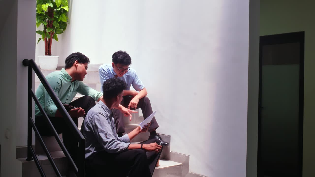 Young student collaborating on ideas while sitting on modern office stairs discussing documents