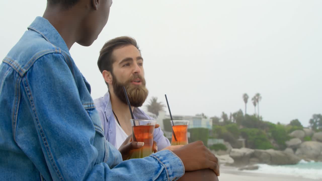 Vista laterale di coppia multirazziale che beve un cocktail in spiaggia 4k