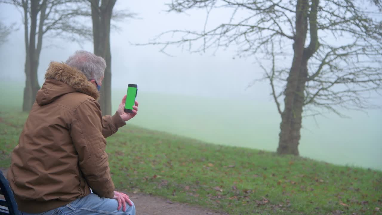 노인 남자가 안개 공원에서 가족에게 비디오 통화를 합니다.