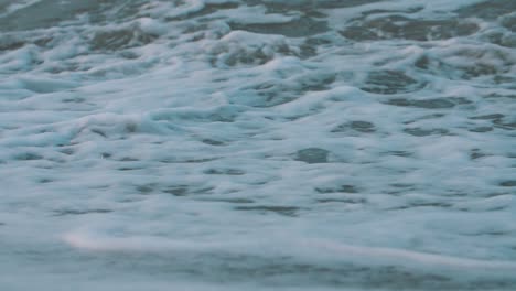 primer plano de la espuma de las olas rompiendo en la arena de la playa en cámara lenta