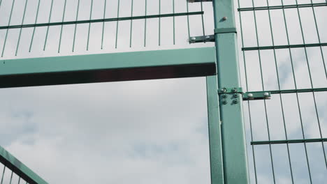 close-up of green metal gate opening, detailed with bolts and hinges, set against clear sky, focus on movement and mechanism, highlighting outdoor sports or urban infrastructure