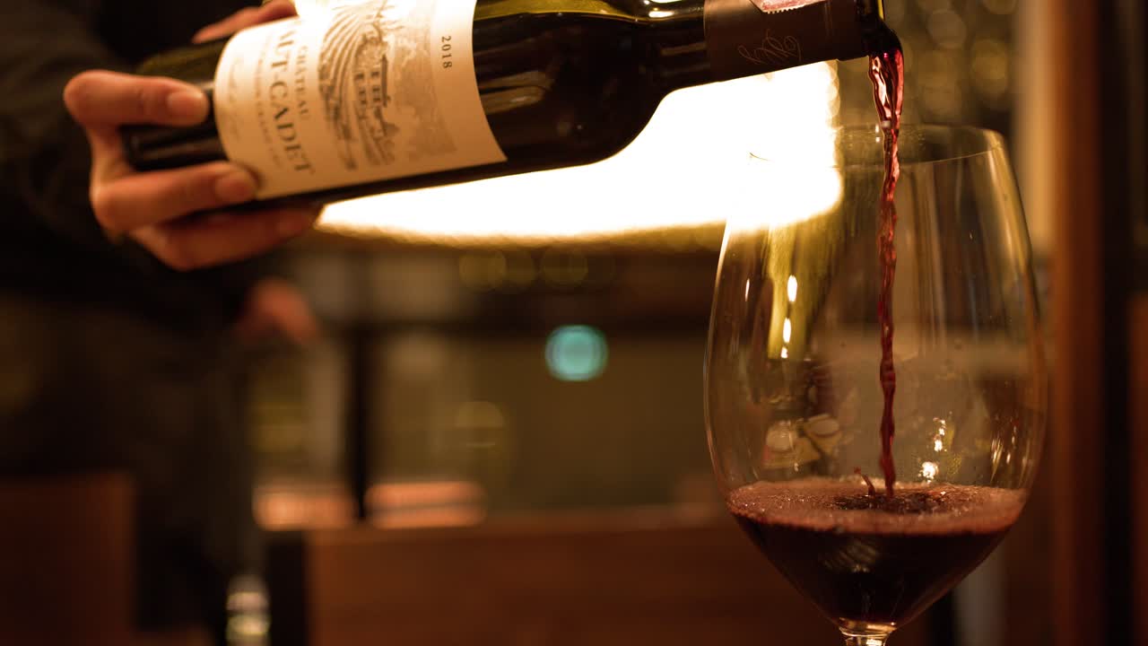 Primo piano di un sommelier che versa vino rosso in un bicchiere con illuminazione calda