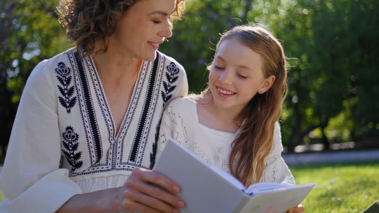 Happy family reading book gathering in cozy garden closeup. Woman girl resting