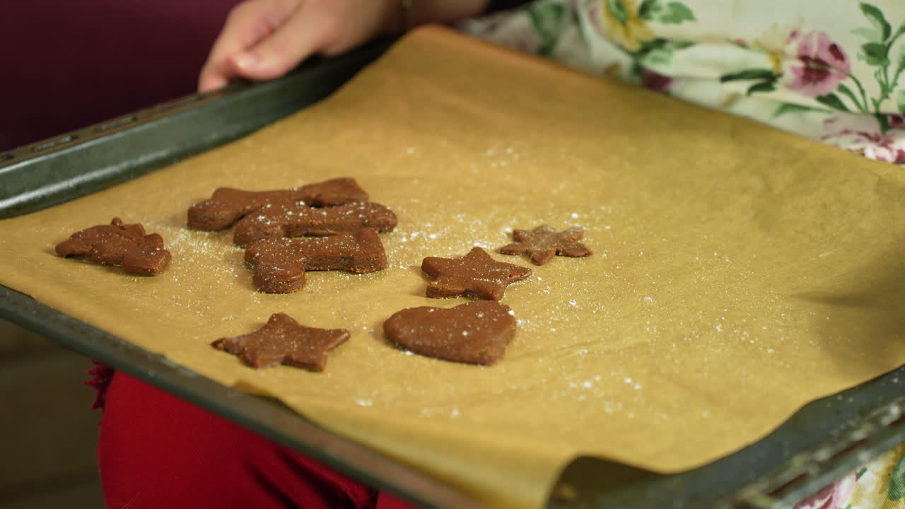 Small hands place star and heart shaped gingerbread cookies on a parchment lined tray lightly dusted with flour ready for baking in a warm cozy holiday kitchen scene for Christmas