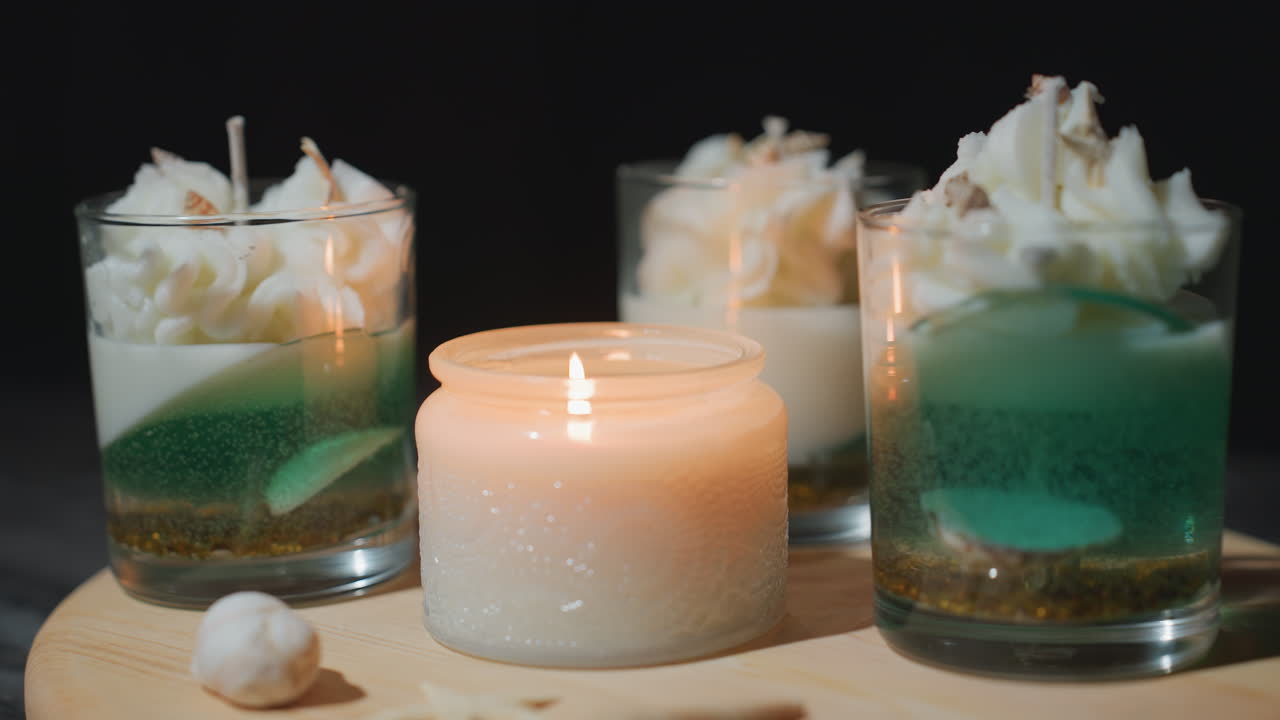 Beautiful decoration featuring candle jar and dessert glasses arranged on wooden stand, illuminated warmly by soft candlelight, creating cozy inviting scene with tiny seashells enhancing charm