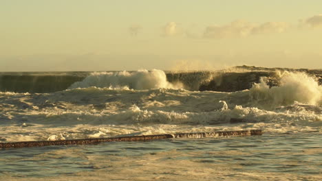 las olas violentas del mar chocan contra la costa rocosa creando un gran chorro durante la puesta de sol dorada.
