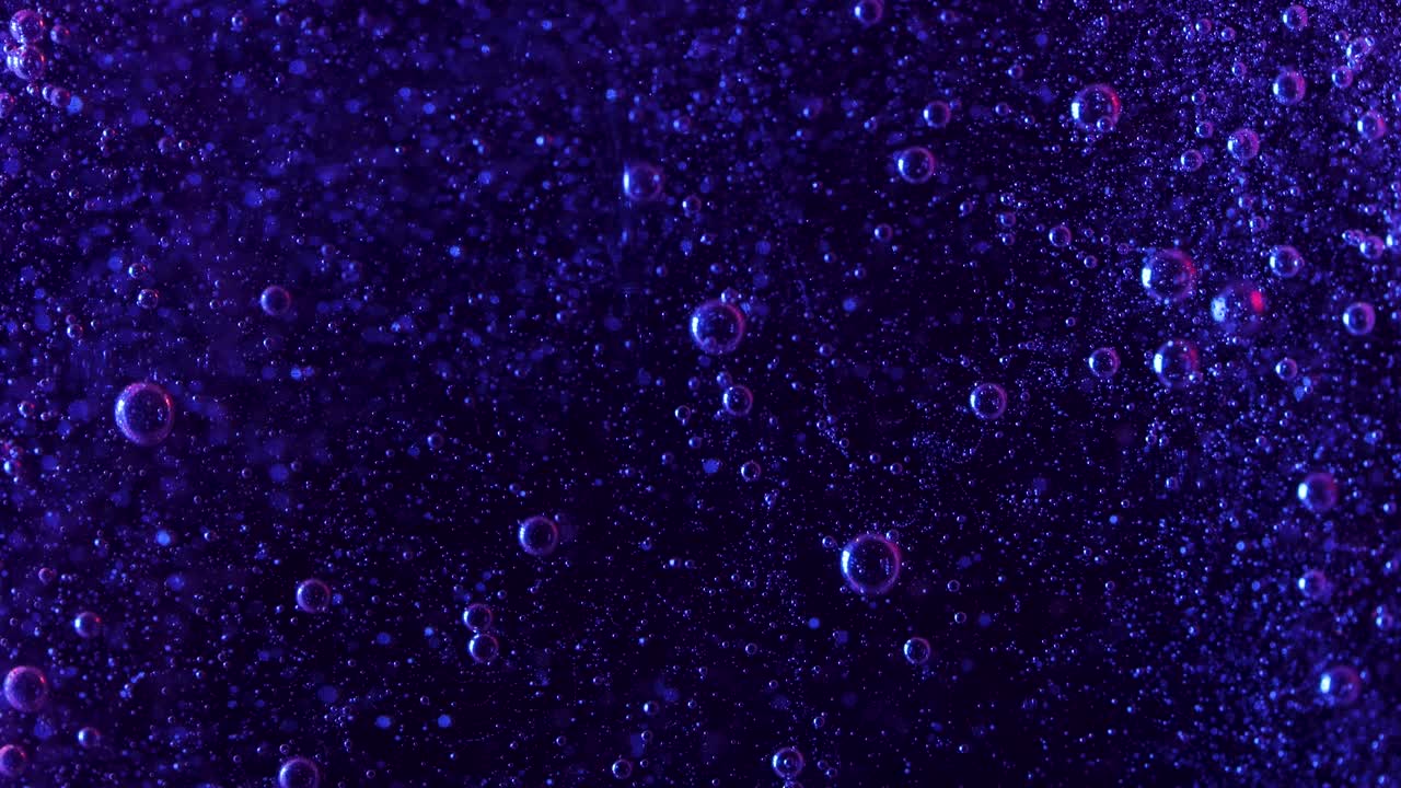 Dark purple bubbles mysteriously rise against a black background as these little spheres rise a cascade of tinier bubbles fall in the background showing the currents created by the larger bubbles