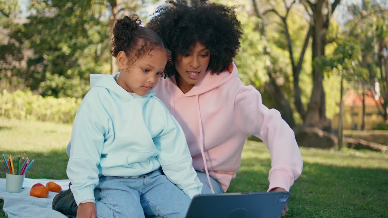 madre hija mirando tableta en el prado verde de cerca. picnic familiar