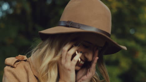 vista de cerca de una joven rubia caucásica con sombrero y hablando por teléfono y riéndose en el parque en otoño