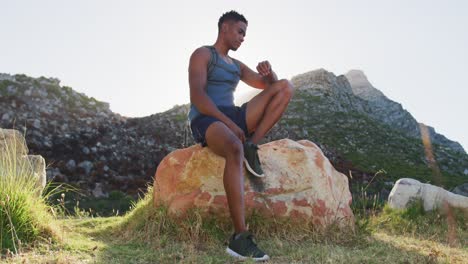 Afroamerikanischer-Mann-Beim-Cross-Country-Laufen,-Sitzend-Auf-Einem-Felsen-In-Der-Berglandschaft