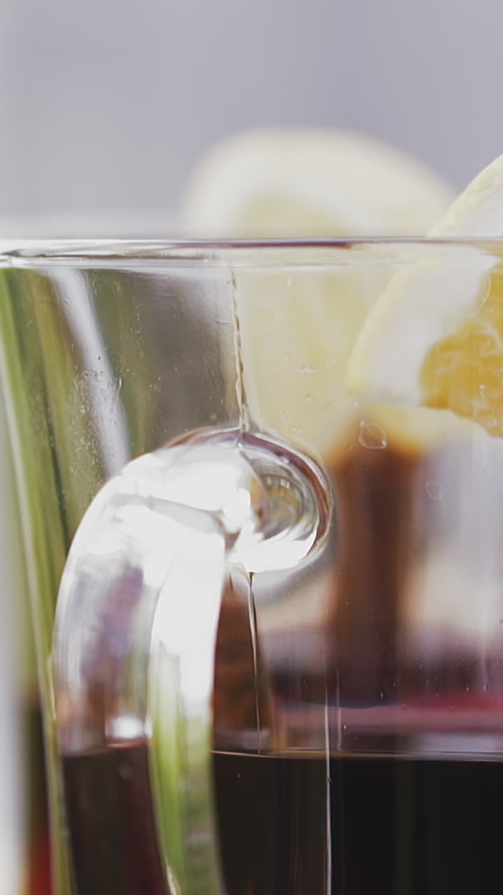 CU shot, slow motion: skilled barman in black gloves puts glass cup with delicious red mulled wine with orange slice on table extreme close view