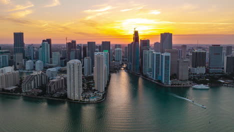 Modern-high-rise-buildings-on-waterfront-against-setting-sun.-Forwards-fly-above-river-estuary.-Hyperlapse-shot.-Miami,-USA