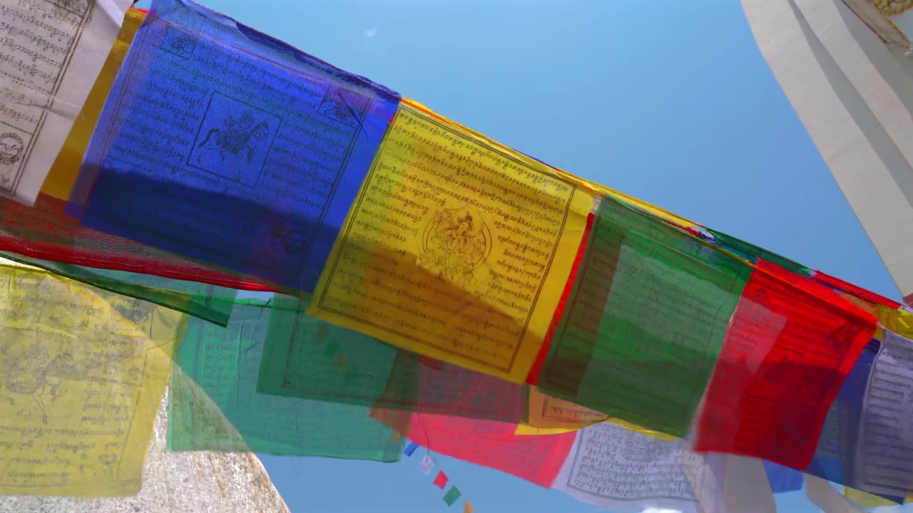 Primo piano dal basso di colorate bandiere di preghiera tibetane iscritte con mantra sacri che sventolano contro un cielo azzurro brillante in un tempio a Kathmandu, Nepal