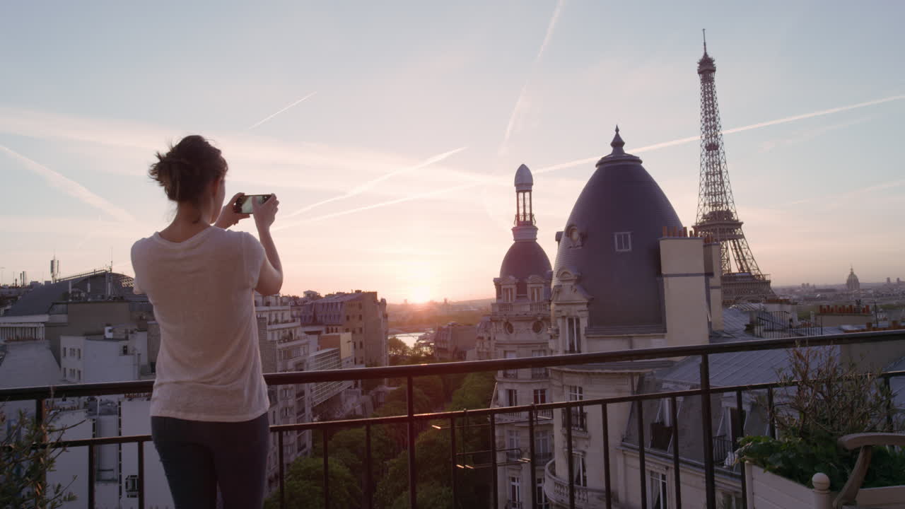 donna felice che usa lo smartphone che scatta foto che si gode di condividere l'esperienza delle vacanze estive a parigi che fotografa la bellissima vista del tramonto della torre eiffel sul balcone