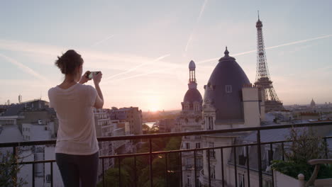 Mujer-Feliz-Usando-Un-Teléfono-Inteligente-Tomando-Fotos-Disfrutando-Compartiendo-Experiencias-De-Vacaciones-De-Verano-En-París-Fotografiando-La-Hermosa-Vista-Del-Atardecer-De-La-Torre-Eiffel-En-El-Balcón