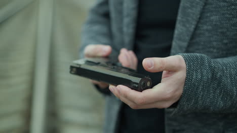 a close view of a man handling a handgun, adjusting the weapon while standing beside a railway track