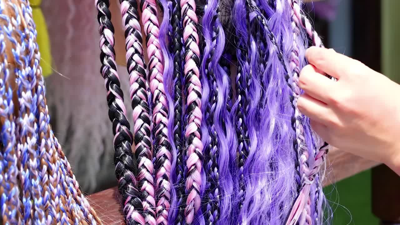 Hands skillfully braid purple and black hair extensions, highlighting detailed patterns and vibrant textures.
