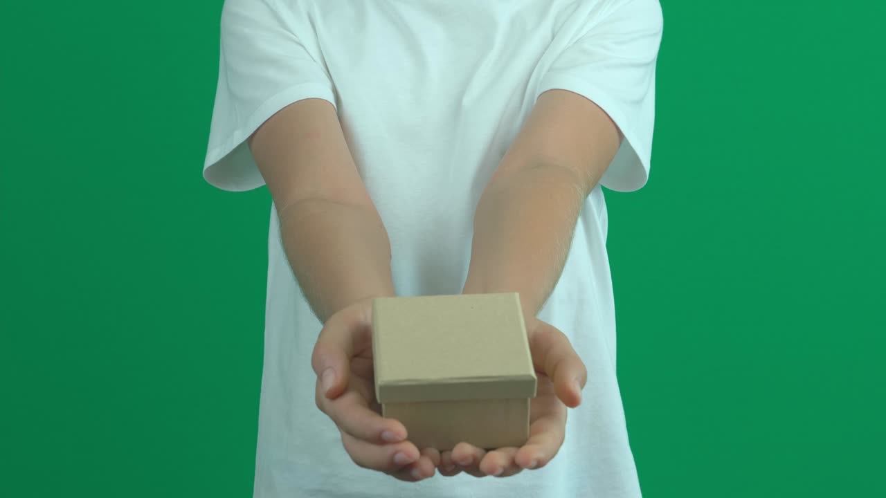 las manos del niño adolescente se estiran y dan una pequeña caja de regalos sobre la pantalla verde.