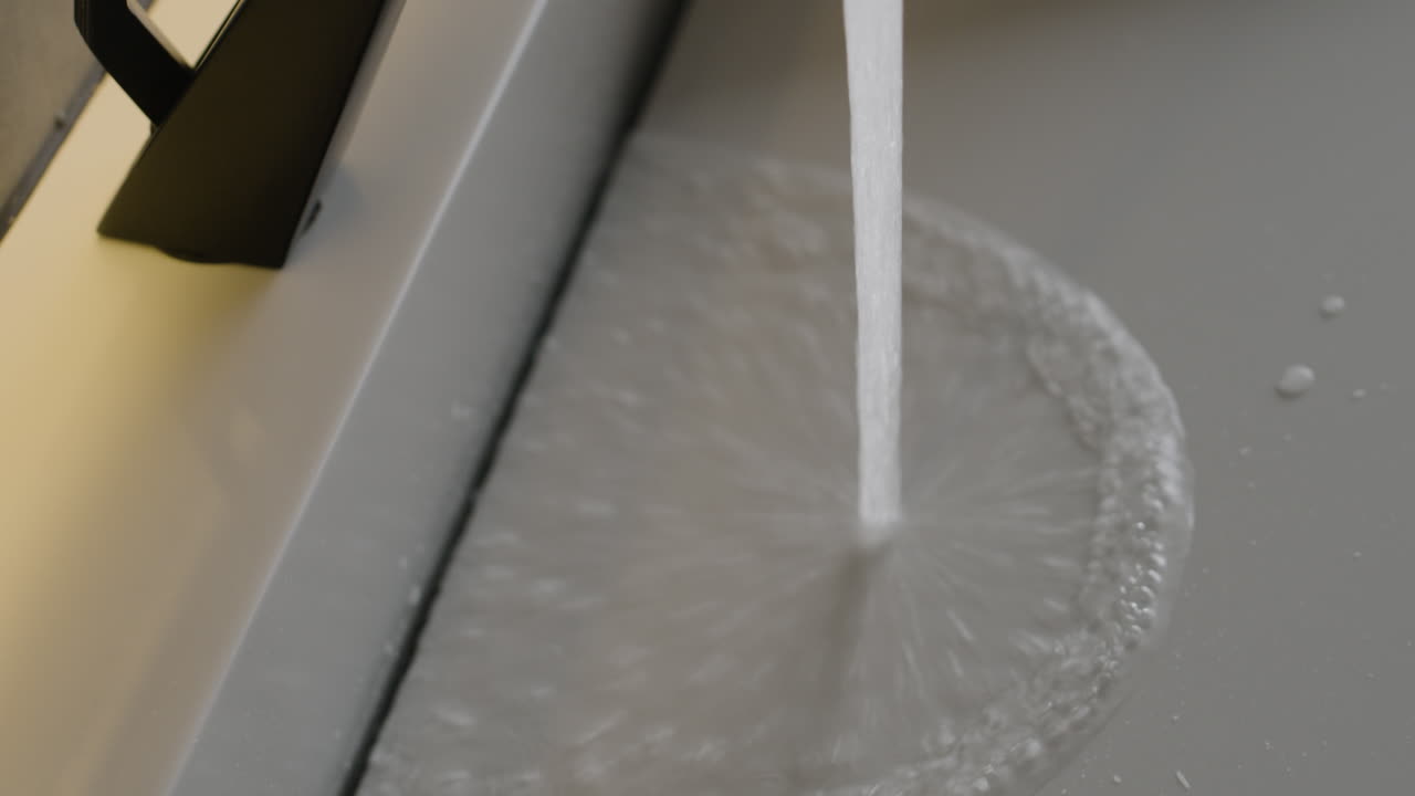 Water flowing from a modern black faucet into a gray sink