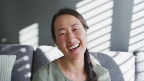 Happy-asian-woman-sitting-on-sofa-close-to-window-at-home