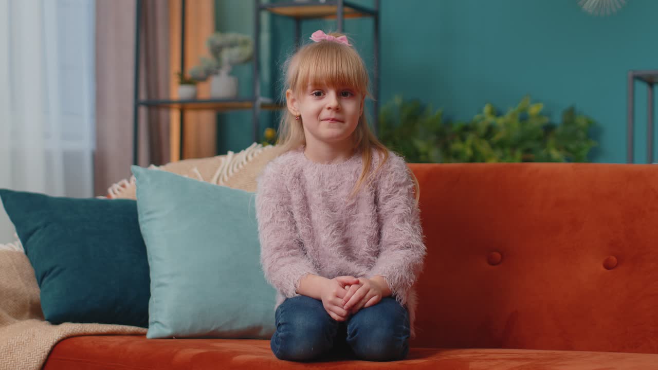 Confused little child girl kid at home having doubts no idea being clueless and uncertain shrugs