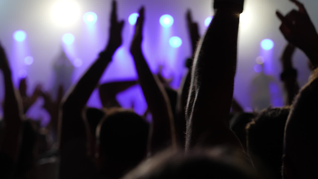 Audience at a live music concert, hands raised in excitement, illuminated by colorful stage lights, creating a vibrant atmosphere of energy and celebration