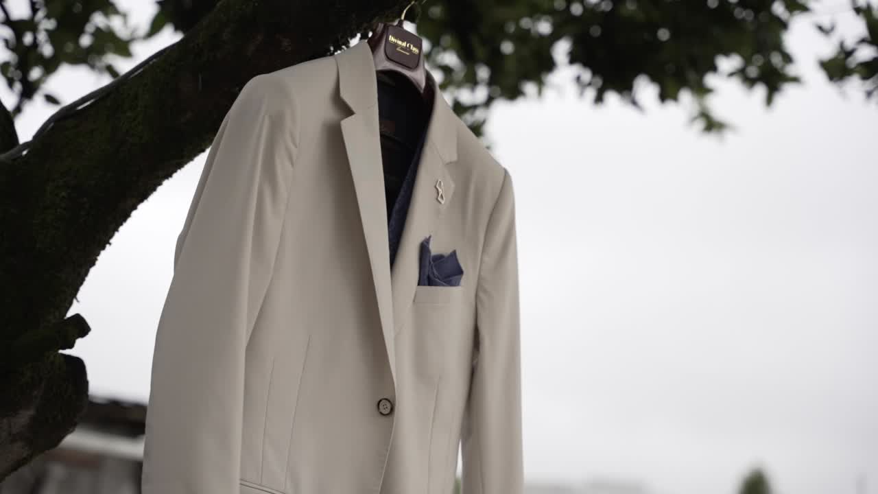 Stylish beige wedding suit with blue pocket square hanging from a tree branch