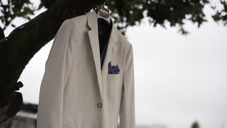 stylish beige wedding suit with blue pocket square hanging from a tree branch