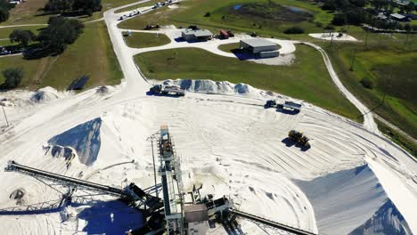 Aerial-view-of-a-sand-mine-where-a-bucket-loader-loads-a-truck-with-material-for-transport,-orbit