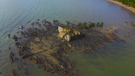 disparo de drones girando alrededor de un frente de roca de una playa tropical durante el día
