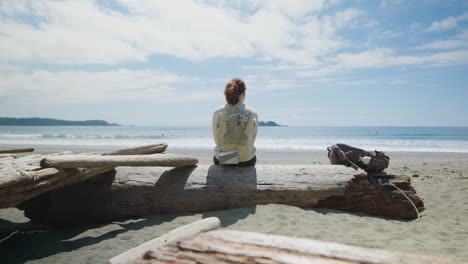 female backpacker on washed up driftwood enjoys beautiful ocean view