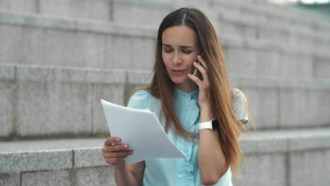 Businesswoman-talking-on-smartphone-at-street.-Executive-looking-on-documents