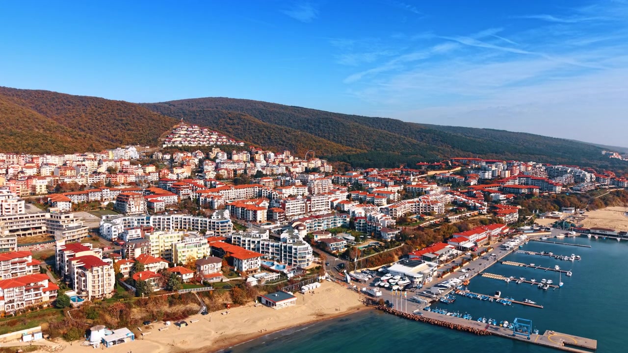 Marina ve kumlu plajı olan sahil kasabasının havadan görünümü, Bulgaristan. Kıyı şeridi boyunca kırmızı çatılı tatil köyü binalarının ve ormanlık dağın drone perspektifi.
