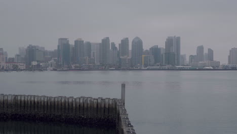 Zooming-in-on-Downtown-San-Diego,-with-beautiful-wooden-poles-in-the-water-as-a-foreground