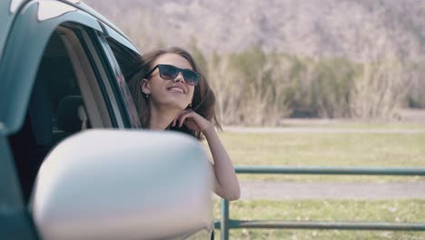 lady in sunglasses fixes hair leaning out of car at field