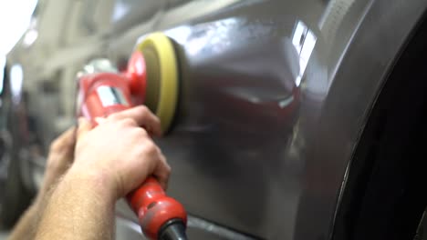 male worker using a polisher to polish a black car