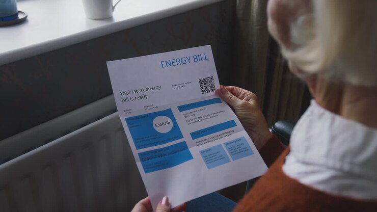 Ældre kvinde i kørestol med energiregning ved radiatoren under energikrisen og stigende leveomkostninger
