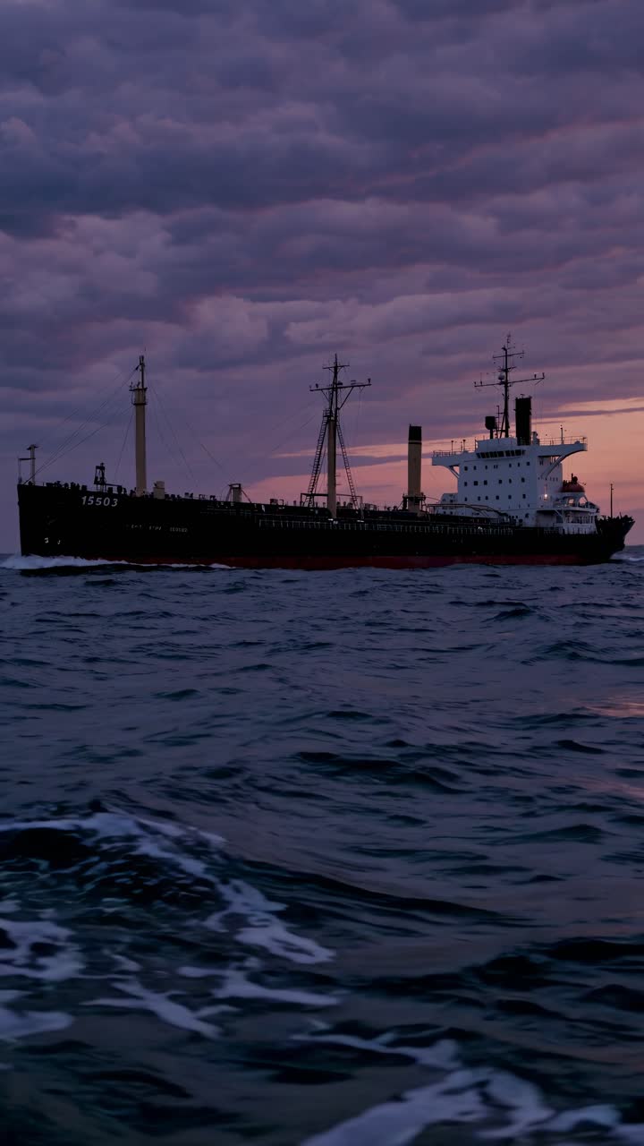 A dramatic video scene of a cargo ship at sunset, captured from a low angle, emphasizing the vast