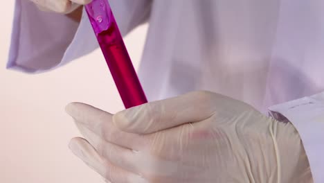 close-up of gloved hands carefully handling a test tube with a vibrant pink liquid.