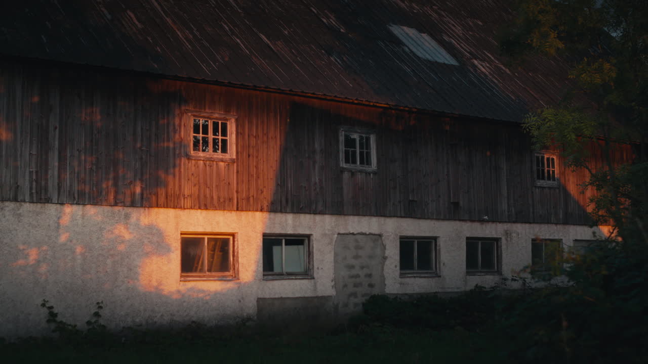 Ein rustikales Scheunenäußeres, aufgenommen während der Goldenen Stunde, mit warmem Sonnenlicht, das weiche Schatten auf das verwitterte Holz und die Betonwand wirft